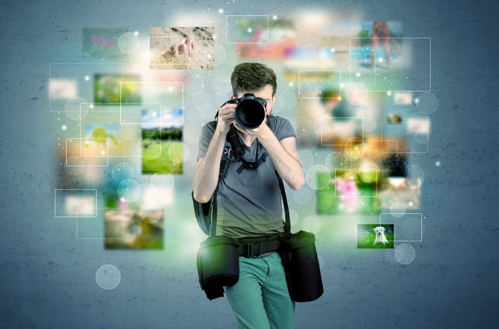 A young amateur photographer with professional camera equipment taking picture in front of blue wall full of faded pictures and glowing lights concept