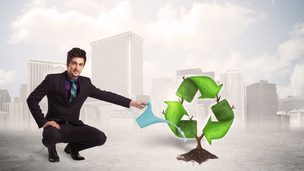 Business man watering green recycle sign tree on city background concept