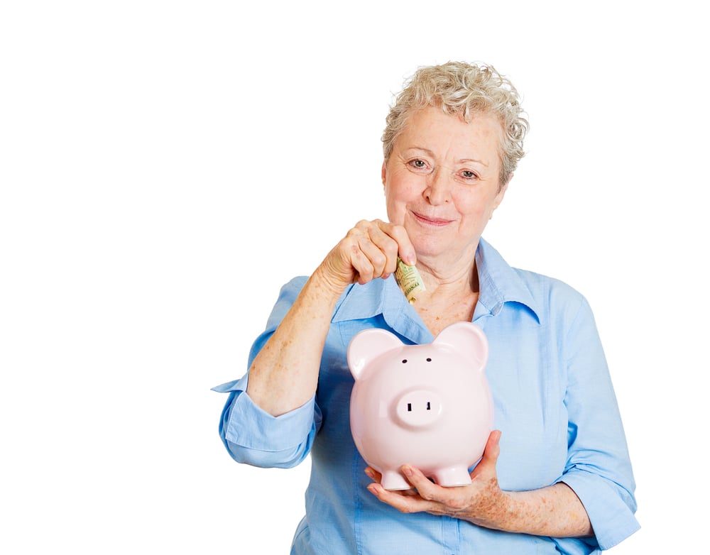 Closeup portrait of smiling senior mature woman depositing money into piggy bank, isolated on white background. Smart currency financial investment wealth decisions. Budget management and savings