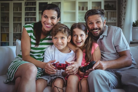 Parents sitting on sofa with their children and playing video games at home