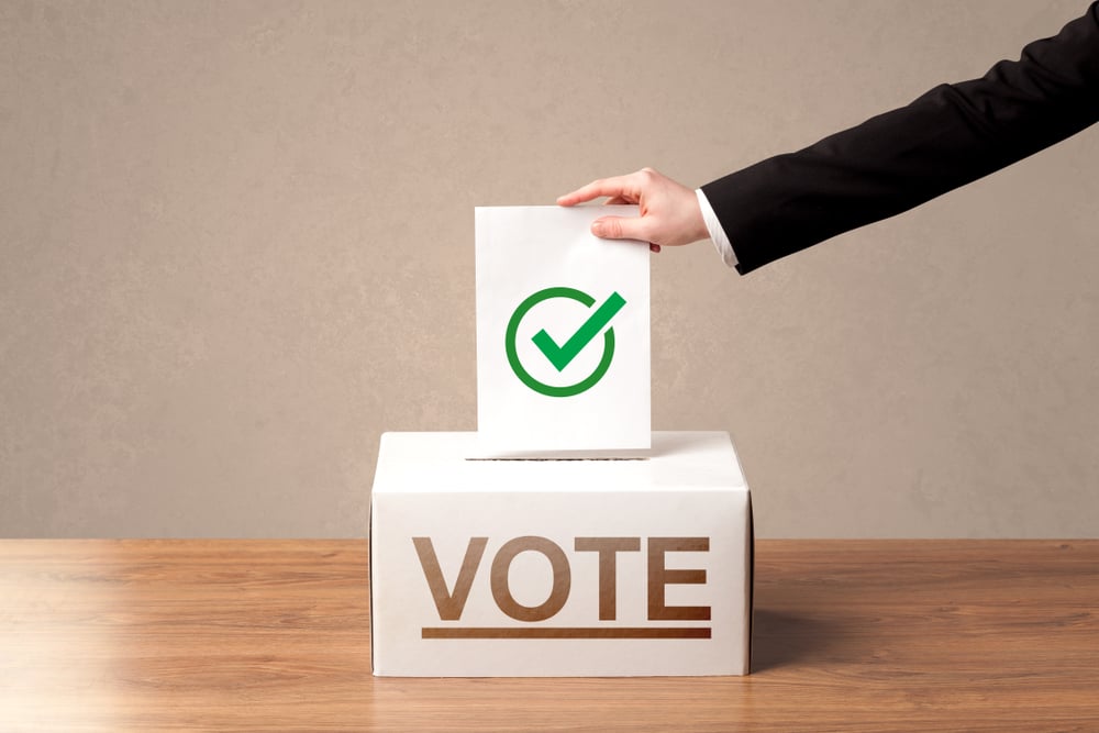 Close up of male hand putting vote into a ballot box, on grunge background